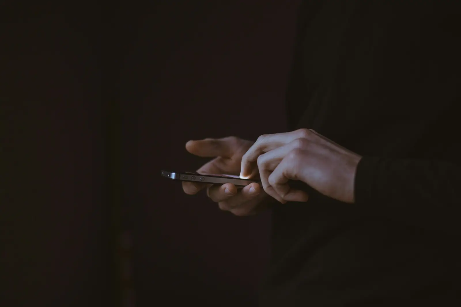 Mani che tengono un telefono in una stanza buia