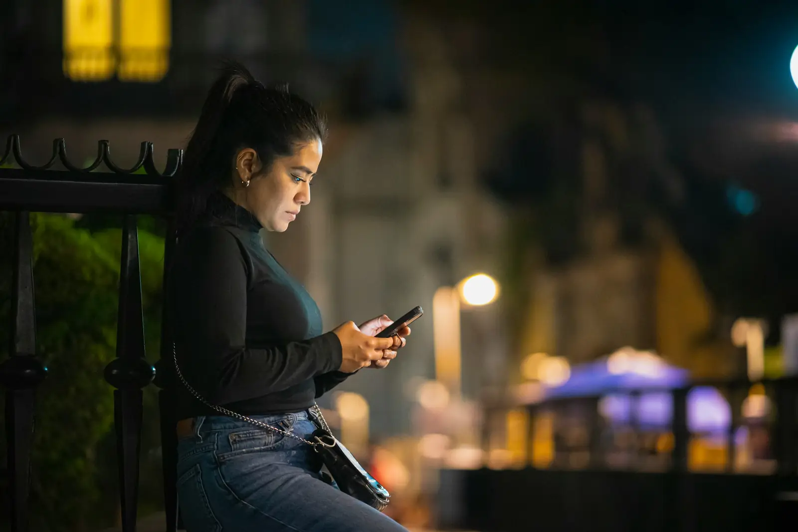 Una donna guarda il telefono in una strada di città, la sera