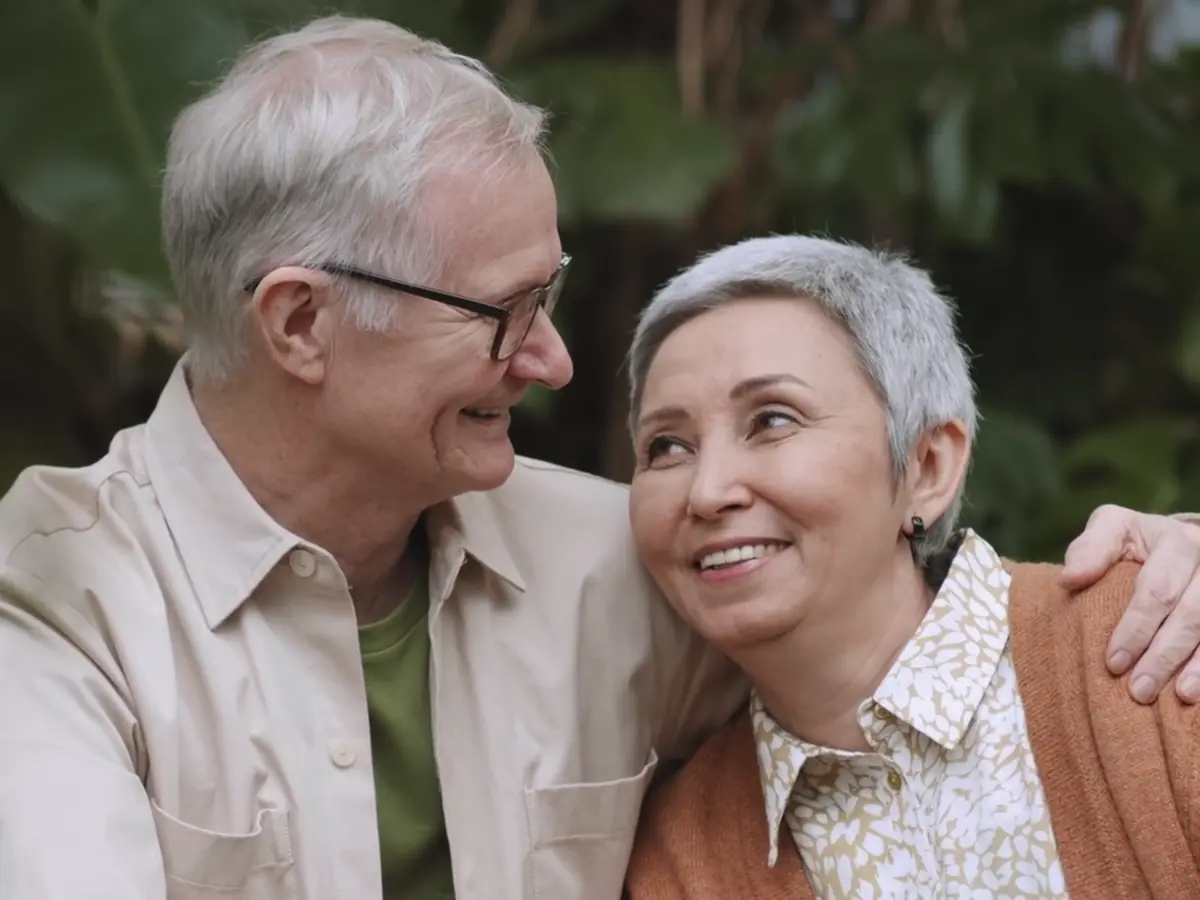 An older couple smiling at each other, his arm round her shoulders