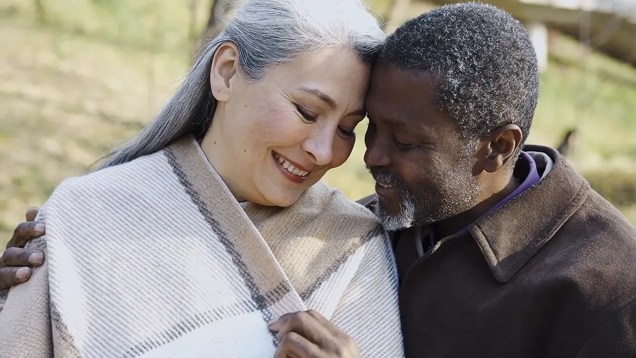An older couple smiling forehead to forehead in a sunny park