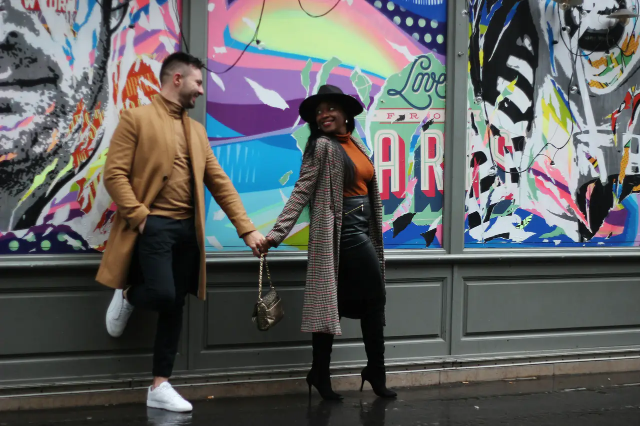 A couple holding hands and laughing in front of a colourful street mural