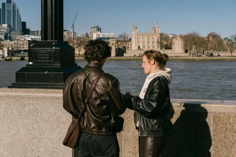Two people talking by the Thames, with the Tower of London across the river