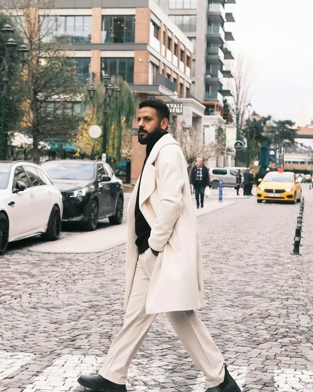 Un homme en manteau long qui traverse une rue pavée